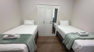 A small, clean room with two single beds, a wardrobe, and a mirror.