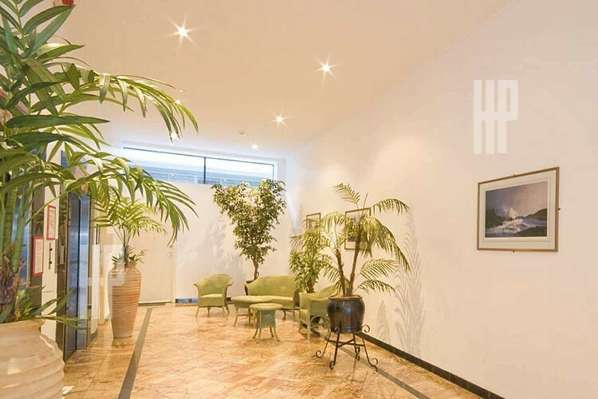 A spacious lobby with a high ceiling, a large potted plant, a seating area with chairs, and a framed picture on the wall.