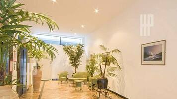A spacious lobby with a high ceiling, a large potted plant, a seating area with chairs, and a framed picture on the wall.
