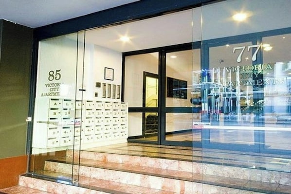 A hotel entrance with a glass facade, numbered apartment signs, and a visible staircase leading inside.