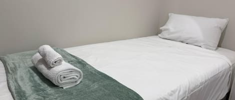 A single bed with a white mattress and a green blanket.