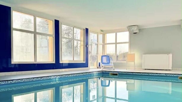 A large indoor swimming pool with clear blue water, surrounded by large windows and a blue wall.