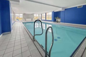 Ein Hallenbad mit klarem, blauem Wasser, Fliesenboden und Metallleiter.