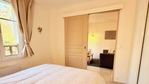 A bedroom with a bed, a door leading to a sitting area, and a window with curtains.