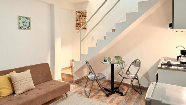 Una sala de estar moderna con un sofá, dos sillones, una mesita y una zona de cocina con estufa.