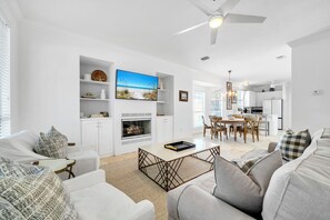 A modern living room with a fireplace, a dining area, and a kitchen. - Coastal Calm, Private Deeded Beach Access, 4 Seater Golf Cart, Bikes, Dogs (Inlet beach)