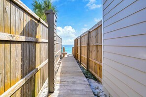 A wooden boardwalk leading to a beach, flanked by wooden fences and a building with a white exterior. - Coastal Calm, Private Deeded Beach Access, 4 Seater Golf Cart, Bikes, Dogs (Inlet beach)