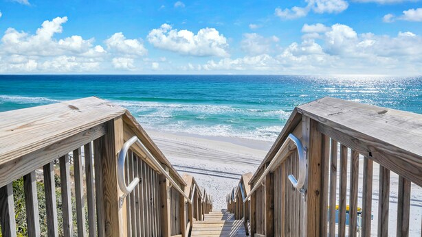 Une promenade en bois qui mène à une plage d’où l’on a une vue dégagée sur l’océan.