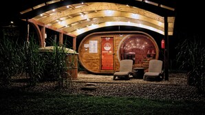 A wooden spa building with a circular interior, two wicker chairs, and a wooden door with signage.