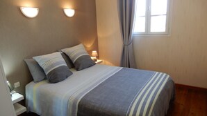 A neatly made bed with striped bedding, two wall-mounted light fixtures, and a window with curtains. - VILLA DES BAINS DE MER 1 A 3 PERS 300 M PLAGE AVEC BALCON ET VUE VELOS FOURNIS (Mers-les-Bains)