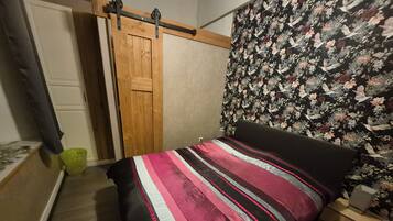 Ein Schlafzimmer mit einem Bett, einem Holzschrank, einer grünen Mülleimer und einer Wand mit Blumenmuster.