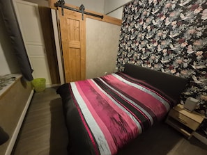 Een slaapkamer met een bed, een houten garderobe, een groene prullenbak en een wand met een bloemenmotief.