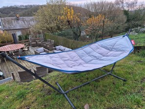 Eine Hängematte auf einer Rasen-Terrasse, im Hintergrund ein Ziegelhaus und Gartenmöbel.