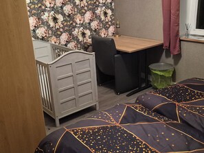 Une chambre comprenant un berceau, un bureau, une chaise, une poubelle et un lit avec une couvre-lit à motifs.