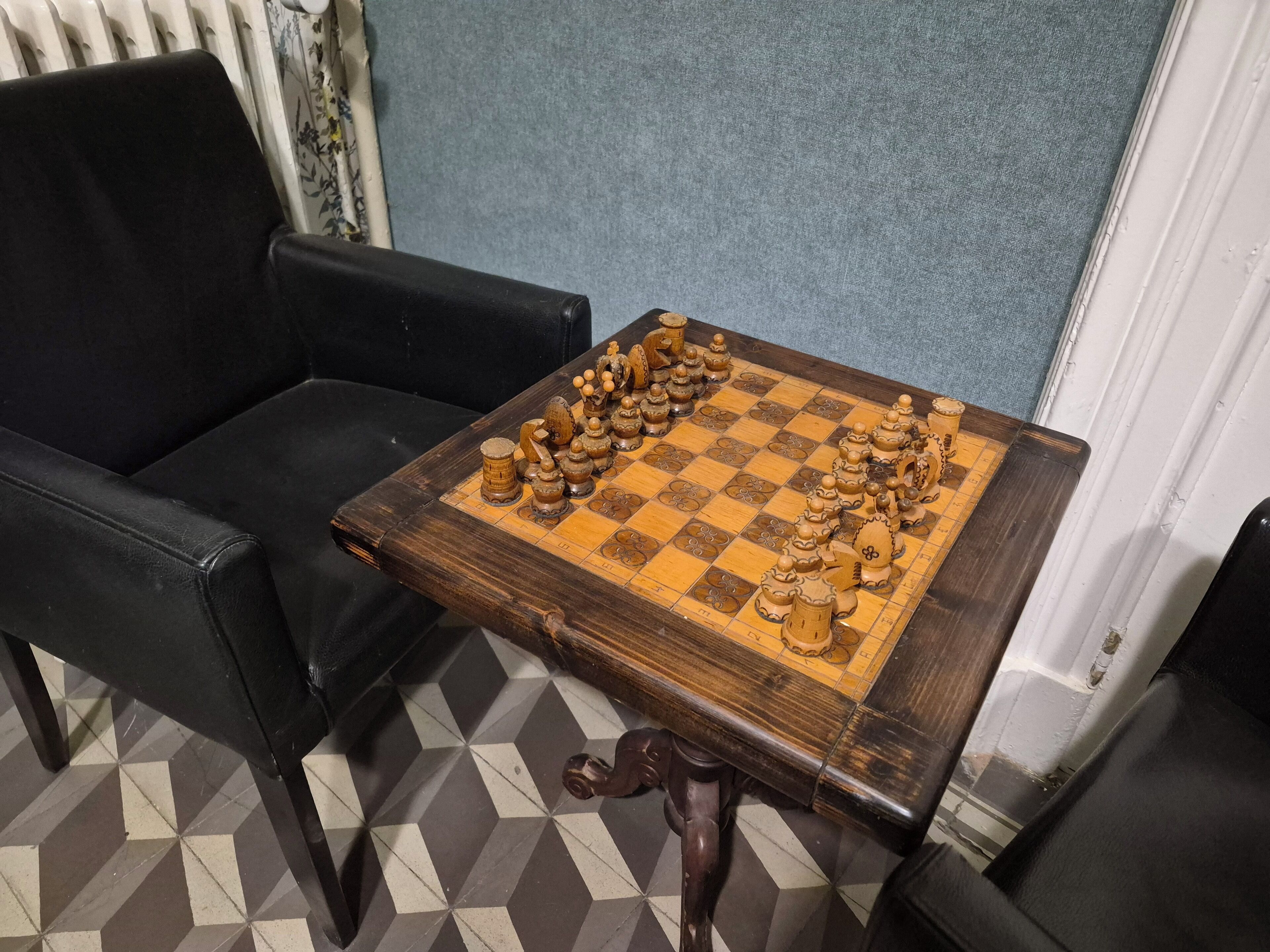 A chessboard on a wooden table with a checkered floor.