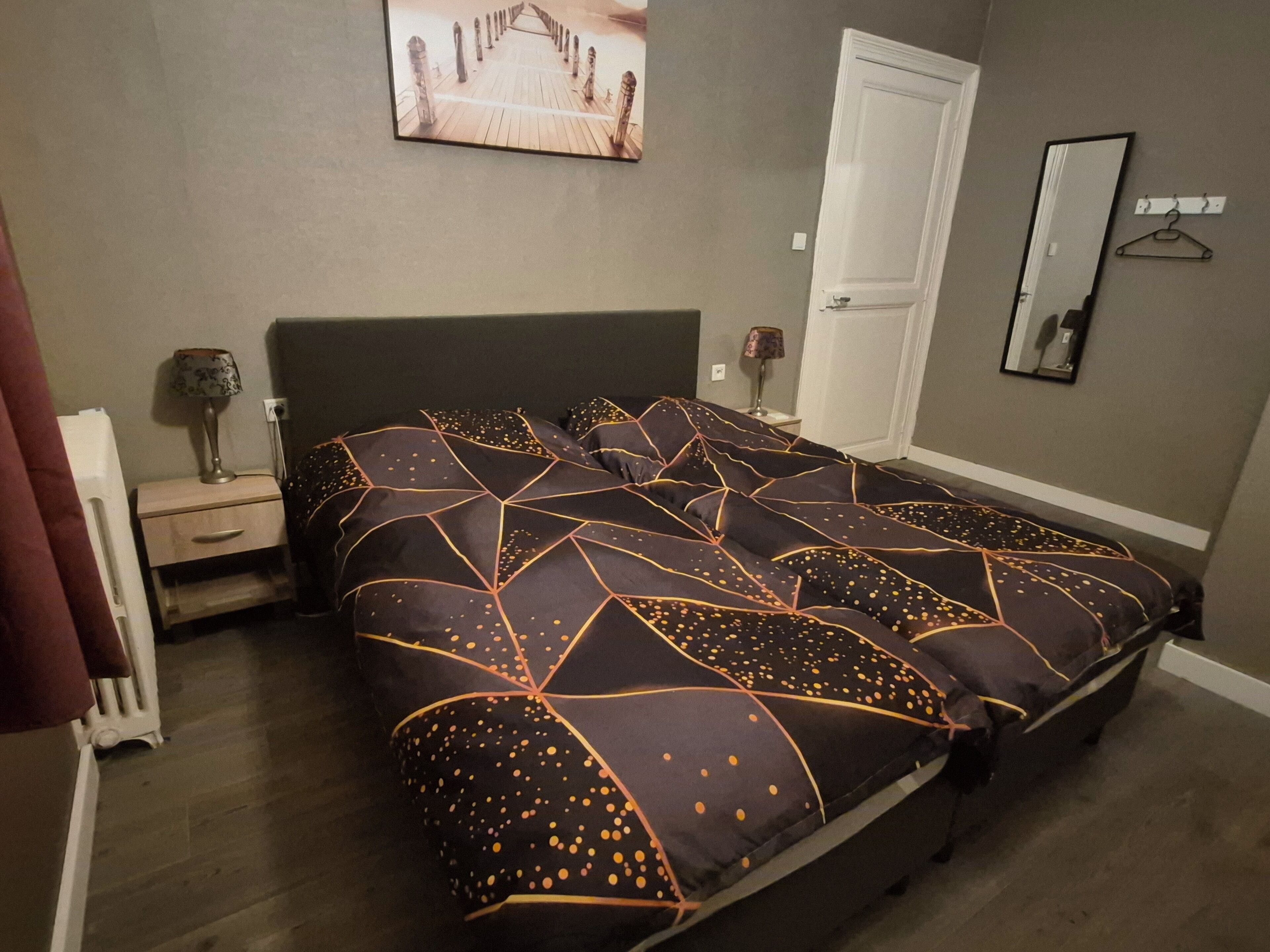 A bedroom with a bed, a nightstand, a lamp, a door, and a mirror on the wall.