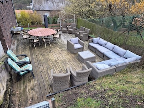Een houten terras met rieten meubels, waaronder een ronde tafel met stoelen, een bank en twee fauteuils.