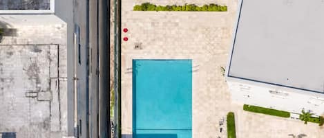 An aerial view of a building with a swimming pool, a parking area, and some greenery.