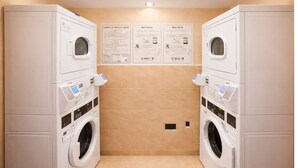 Una sala de lavandería con dos lavadoras apiladas, un panel de control y carteles instructivos en la pared.