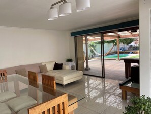Un salon moderne avec une table à manger en verre, un canapé et une vue sur un jardin avec une piscine.