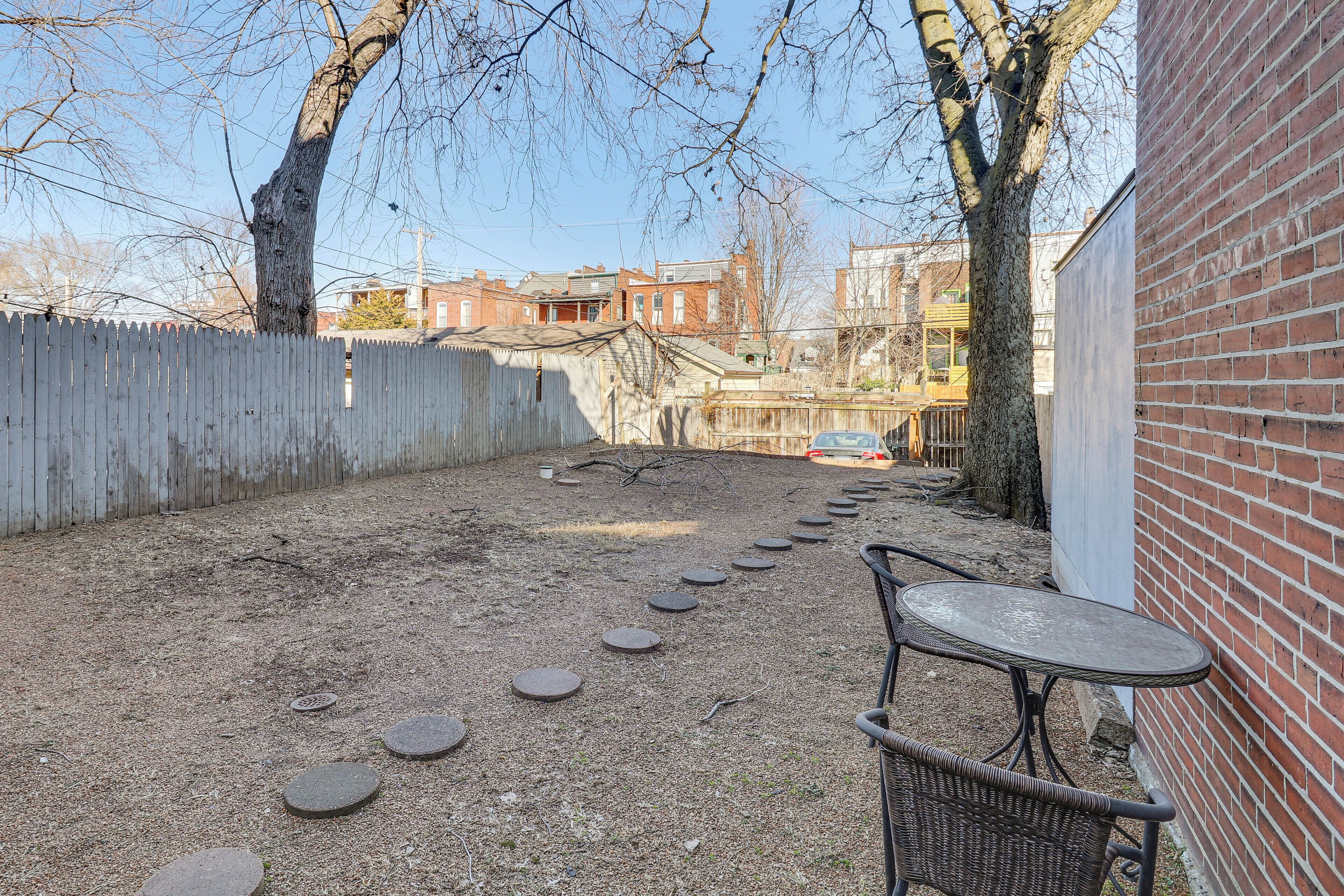 Un espacio al aire libre con piso de adoquines, pared de ladrillo, mesa de metal y silla de mimbre.