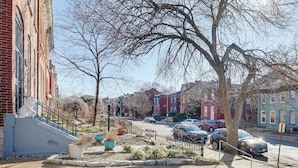Uma rua residencial com casas de tijolo, uma estátua de leão de pedra e calçada arborizada.