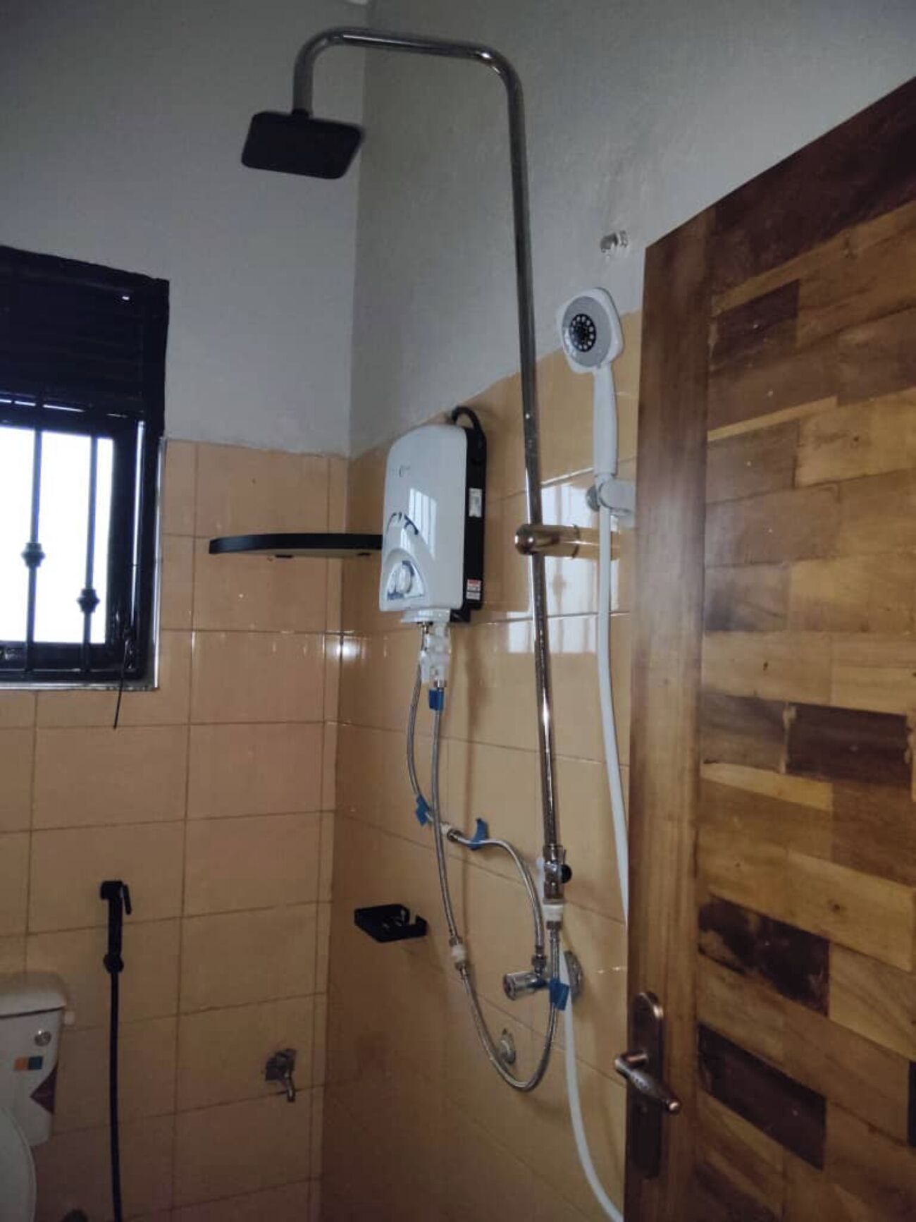 A shower area with a handheld showerhead, a wall-mounted faucet, and a toilet visible in the corner.
