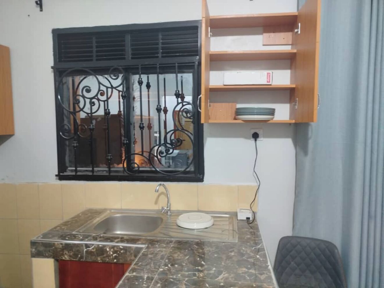 Una cucina compatta con lavello, piano di lavoro e finestra con inferriate decorative.