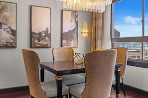 Ein Essbereich mit Tisch und Stühlen, Bilderrahmen an der Wand und Blick auf die Stadt durch ein großes Fenster.