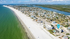 Vue aérienne d’une ville côtière avec une longue plage de sable, un port de plaisance et des immeubles résidentiels.