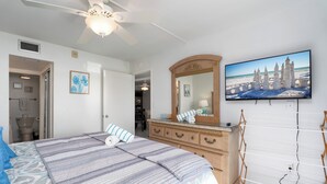 Une chambre à coucher avec un lit, une commode, un miroir et un téléviseur fixé au mur.