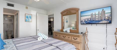 A bedroom with a bed, dresser, mirror, and a television on the wall.