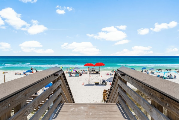 A wooden boardwalk leading to a beach with umbrellas and beach chairs.