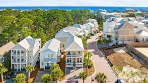 A coastal residential area with multiple two-story houses, a paved road, and a view of the ocean. - 30A Home for 10: Pool, Golf Cart & Chef's Kitchen, Open-Concept Living (Santa Rosa Beach)