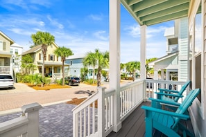 A residential street with houses, a porch with blue chairs, and a clear blue sky.