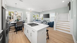 A modern kitchen with a central island, dining area with chairs, a staircase, and a living room with a sofa. - 30A Home for 10: Pool, Golf Cart & Chef's Kitchen, Open-Concept Living (Santa Rosa Beach)