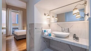 Un baño moderno con un lavamanos grande de mármol, un espejo con luces empotradas y una zona de ducha.