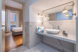 A modern bathroom with a large marble sink, a mirror with wall-mounted lights, and a shower area. - Navona Boutique House (Roma)