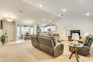 A modern living room with a sofa, a coffee table, and a TV. There is a kitchen in the background with white cabinets and a microwave. - Screened Lanai - Relaxing Retreat in Ocala (Ocala)