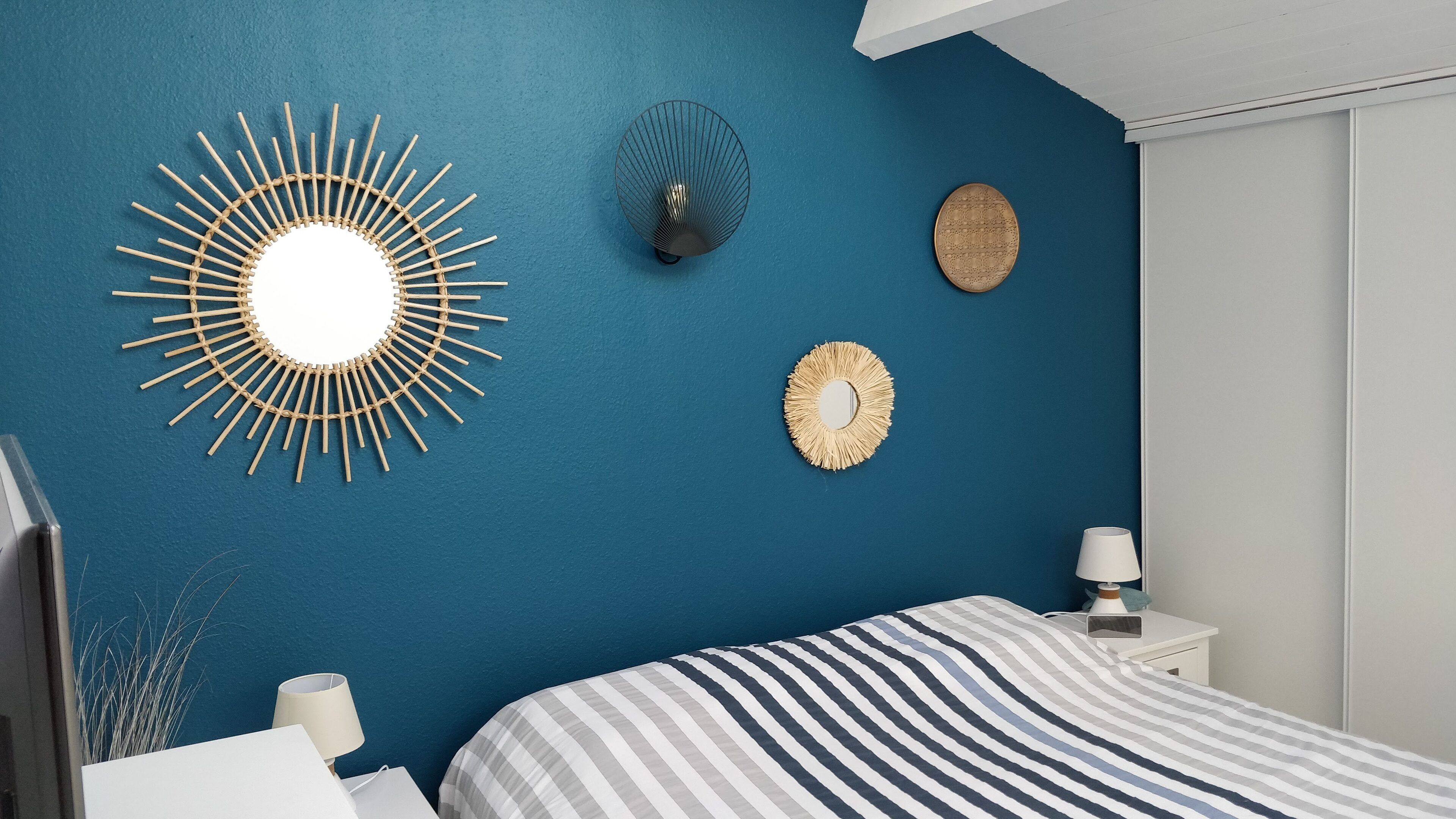 Une chambre avec un mur bleu, un lit avec une literie à rayures et trois objets décoratifs fixés au mur.