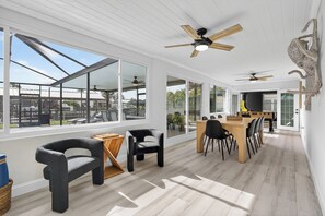 Ein geräumiges Zimmer mit großen Fenstern, einer Essecke mit Holztisch und -stühlen sowie Deckenventilatoren.