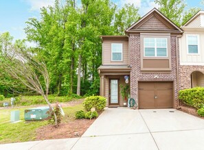 A two-story house with a brick facade, a garage, and a well-maintained lawn. - 3-bedroom Modern Townhome in charming Lithonia! (Lithonia)