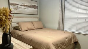 Una camera da letto con un letto, un comodino, un vaso con fiori secchi, un quadro appeso alla parete e una finestra con persiane.