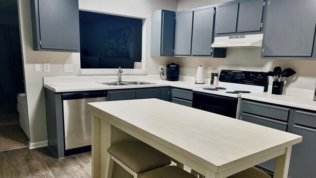 Una cucina moderna con mobili grigi, un piano di lavoro bianco e un tavolo in legno con due sgabelli.