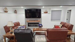 Ein modernes Wohnzimmer mit Ledersofas, einem Holztisch, einem an der Wand montierten Fernseher und Dekorationselementen wie einem Globus und Schiffmodellen.