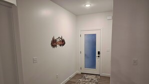 Ein Flur mit Holzboden, einer weißen Tür mit geätztem Glasfenster und einem kleinen Kunstwerk an der Wand.