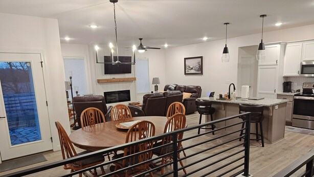 Eine moderne Küche mit Edelstahlgeräten, ein Essbereich mit Holztisch und -stühlen sowie ein Wohnzimmer mit braunem Ledersofa und Flachbildfernseher.