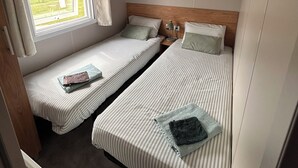 A compact room with two single beds, a window with curtains, and a small shelf with a decorative item.