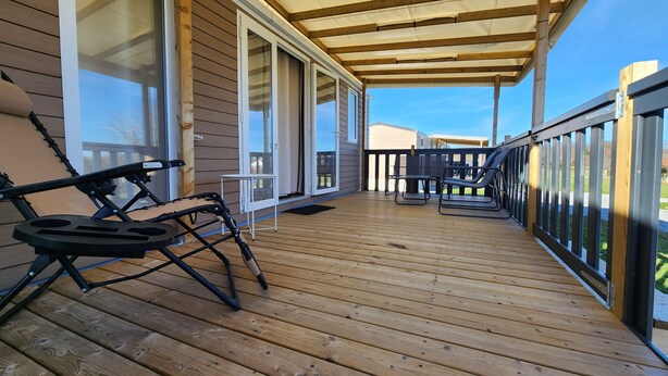 A wooden deck with a covered area, sliding glass doors, and outdoor furniture.