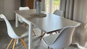 A dining area with a white table, two white chairs with wooden legs, and a vase with branches.
